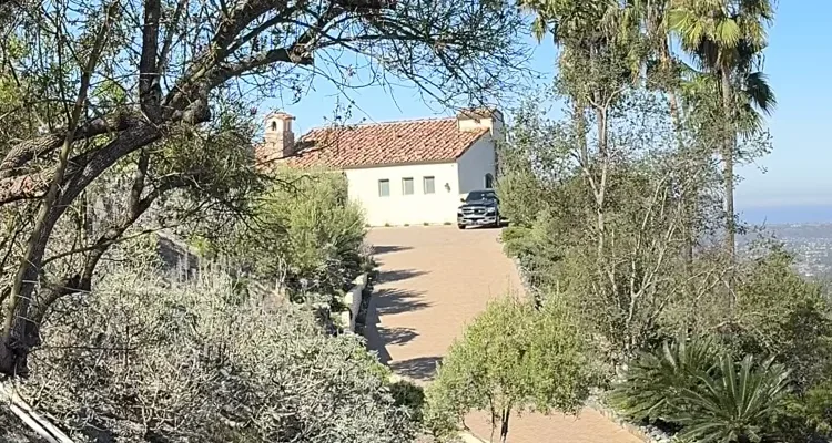 A long paver driveway climbing to the motor court of a tile-roofed estate in Cielo, Rancho Santa Fe, with the coastal haze beyond