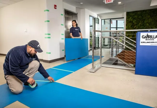 Gorilla Movers crew laying floor runners and wall protection in a San Diego building lobby before a high-rise move