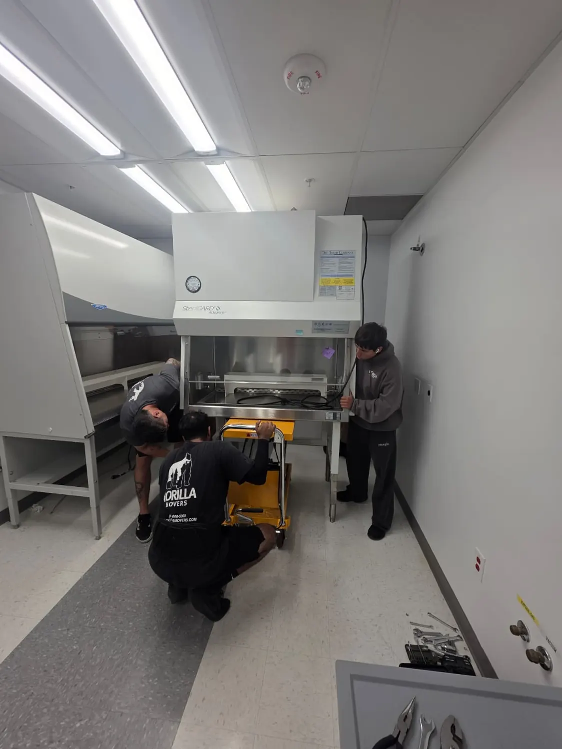 Crew easing a SterilGARD biosafety cabinet onto a hydraulic lift table during a San Diego lab relocation